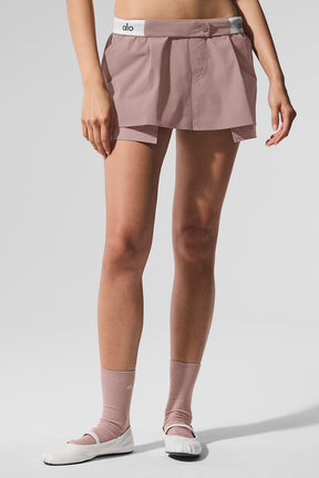 Woman wearing Flip It Mini Skort in pink with elastic waistband and ALO logo, showcasing skort design.