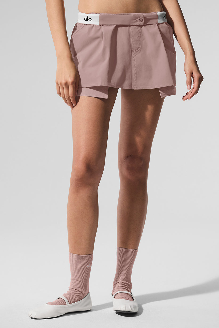 Woman wearing Flip It Mini Skort in pink with elastic waistband and ALO logo, showcasing skort design.